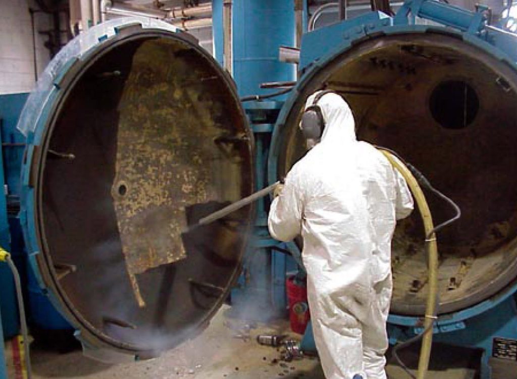 Man in protective gear dry ice blasting large machinery.